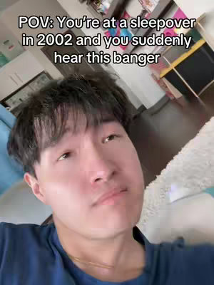 A selfie-style video with the creator in the foreground. He's facing the camera with a slight, almost contemplative expression. The setting looks lived-in, suggesting a casual, home environment, with a mix of furniture and decor visible in the background. The lighting appears natural, with a soft glow on the creator's face.