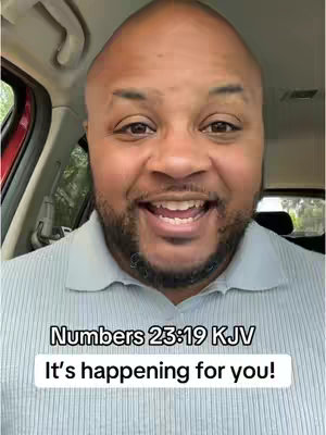 A close-up shot features a Black man inside of a car. He is smiling broadly, with his mouth open as if he is speaking. He's wearing a light-colored, collared shirt. The background is blurred, but suggests a seat and a windshield.