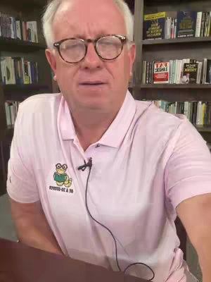 A man wearing glasses and a pink polo shirt appears to be speaking. He is in front of a bookshelf filled with books.