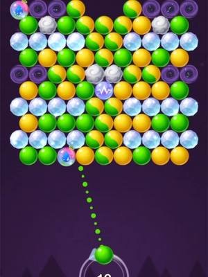 The image is a screenshot of a bubble shooter game. A grid of multicolored bubbles fills the top portion against a dark purple background, with three circular purple shapes on the top, four circular elements in the background and a shooter mechanism at the bottom. A green ball is being fired. The image is centered and well-composed, designed for visual appeal for a game setting.