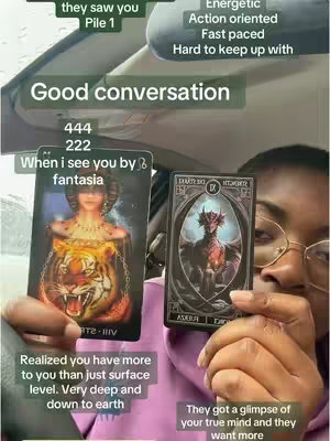 The cover image features a person holding two tarot cards. The person is wearing glasses and a pink top, with their face visible. The cards are in focus, positioned in front of the person. Text overlays are arranged around the cards. The background is interior of a vehicle. The overall composition is designed to attract interest in tarot card readings for spiritual guidance.