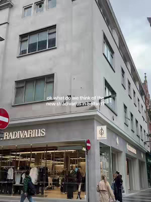 The cover image shows a building on a city street. The building has a Stradivarius storefront on the ground floor, with the building's exterior being a light gray. The street is framed by the building's sharp geometric lines and angled facades. Signs direct traffic, and other shops and passersby fill the background.