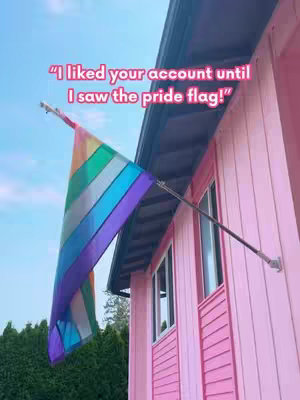 The image shows a pink building with a rainbow pride flag hanging from it. Text is overlaid, indicating the image's message focuses on the flag.