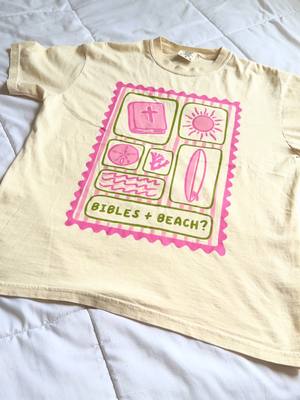 The image shows a T-shirt with a print of a pink postage stamp style design on an off-white fabric. The stamp includes various icons: a book with a cross, a sun, a seashell, seaweed, and a surfboard. The text 'BIBLES + BEACH?' is written at the bottom of the design.