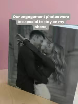 A monochrome photo shows a couple embracing, their faces close together. The man is wearing a dark top. The woman has long hair. The photo is displayed as a spread in a photo book, which is shown at an angle.