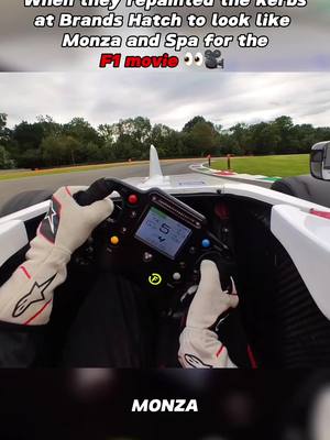 A first-person perspective from inside a race car, showing a driver's hands on the steering wheel and the track ahead. Text overlays are at the top and bottom, communicating information about the scene.