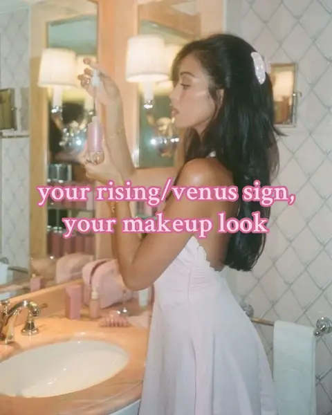 A woman in a pale pink dress stands in a bathroom, applying makeup. The bathroom has a vintage aesthetic with peach-colored walls, marble countertops, and large mirrors. Text overlayed on the image reads, "your rising/venus sign, your makeup look."