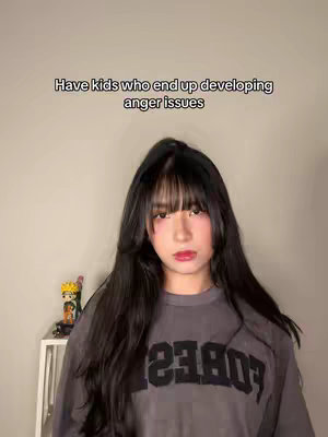 A young woman with long black hair and a grey shirt is centered in the frame. The background is a light neutral color. Text overlay at the top reads, “Have kids who end up developing anger issues.” A cartoon figurine is visible on a shelf to the left.