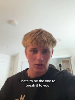 A young man with short blond hair is centered in the frame, facing the viewer. Above him are bright ceiling lights. At the bottom, a text overlay reads, 'I hate to be the one to break it to you.'