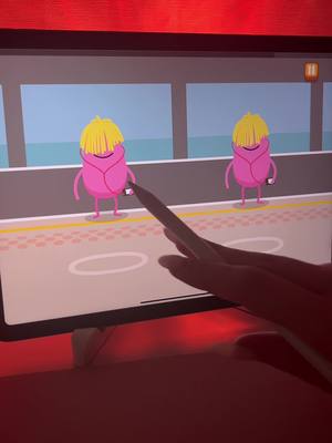 The cover image shows a hand with a stylus pointing toward a tablet screen displaying a cartoon scene. Two pink, bean-shaped characters with yellow hair are in the center, holding phones. The background is a stylized cityscape with blue sky and a gray wall. The overall composition is simple and inviting.