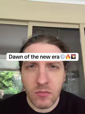 A man with light skin and brown hair is centered in the frame, looking directly at the camera with a serious expression. Above him, an opaque rectangular box contains the words 'Dawn of the new era' in all lowercase, followed by three emoji: a cloud, a flame, and a sun. The background subtly features closed blinds and foliage, providing context for the indoor setting of the selfie-style video.