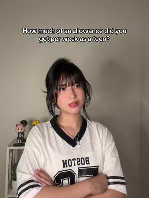 A young woman with dark hair and bangs is centered in a medium shot. She's wearing a white jersey with black stripes and lettering that says 'BOSTON' on the front. Her arms are crossed. Above her, text asks, 'How much of an allowance did you get per week as a teen?' The background is a plain beige wall.
