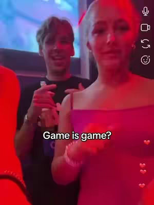 An inside view captures a man and woman in what appears to be a social setting, illuminated by a vivid red glow. The man in the background is slightly out of focus, while the woman in the foreground is more defined, wearing a pink top. The image has overlaid text at the bottom center.