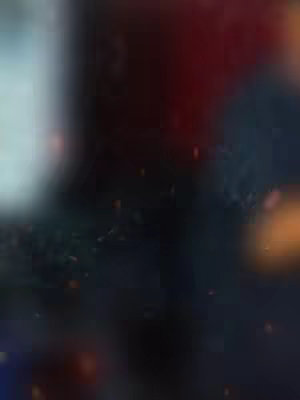 An abstract, blurred image dominated by dark colors with hints of red, white, and orange. A bright spot of white or very light color is in the upper left, while red is more pronounced near the upper right and orange appears towards the bottom right. The overall composition is dark and atmospheric, possibly suggesting a spiritual or dramatic theme.