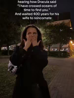 A woman stands on a sidewalk at night, hands covering her face, with text overlayed. The background includes trees, streetlights, and city buildings.