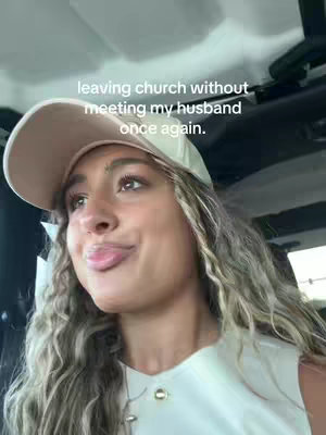 A woman wearing a baseball cap is sitting inside of a car, looking into the camera with a playful expression. Text overlayed on image.
