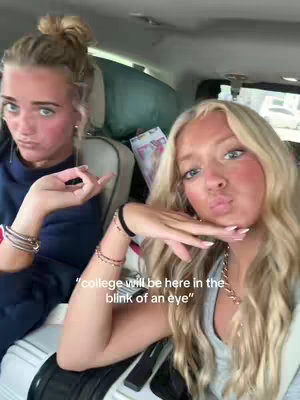 Two young women in the front seats of a car. One is holding her finger up to make a gesture, and the other is resting her face on her hand. Both are looking at the camera. There is text overlaid on the image.
