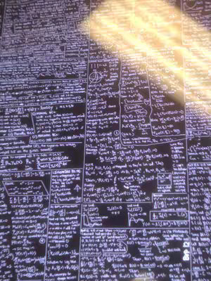 A close-up shot of a screen filled with mathematical equations and formulas, written in white against a dark background. Bright light emanates from the top right corner, partially obscuring the text.