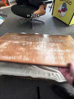 The cover image shows an interior scene, likely a desk or table setting. A wooden surface is prominently featured, with a blurred background showing the surrounding elements, including a person’s hand holding up or presenting the wooden surface. The setting is likely a home or office.