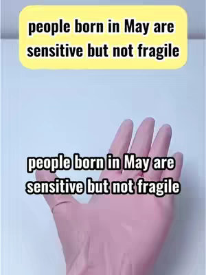 The image displays a hand with pink skin and a light blue background. Two text boxes with rounded edges are visible, one at the top and one at the bottom, both containing the text 'people born in May are sensitive but not fragile'. The hand is positioned in the center, palms facing towards the viewer.