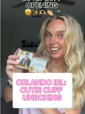 A woman with long blonde hair smiles while holding two small boxes, one with a picture of Harry Potter. The boxes are in front of a white sign that says 'ORLANDO IRL: CUTIE CUFF UNBOXING'. Above the woman's head are the words 'CUTIE CUFF OPENING' in a white script.