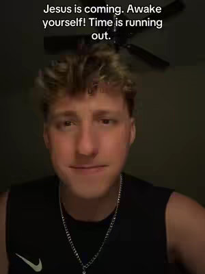 A young man with short, styled blonde hair is centered in a medium shot, facing the camera. He's wearing a black tank top and a silver chain. The background is a dark room with a ceiling fan visible near the top. Overlaid at the top is a white text that reads: "Jesus is coming. Awake yourself! Time is running out."