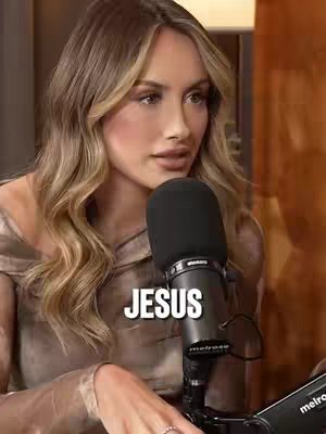 A woman with long blonde hair is holding a microphone and looking to the side. The word "JESUS" is overlaid on the image in a bold, white font.