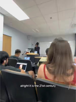 The video shows a classroom with students and a professor giving a lecture. The focus is on a student in the foreground and the professor at the front of the class.
