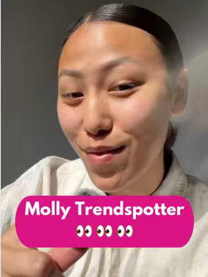 A selfie-style shot of a woman smiling, with a pink banner overlaying her image; the background appears to be a plain grey wall.