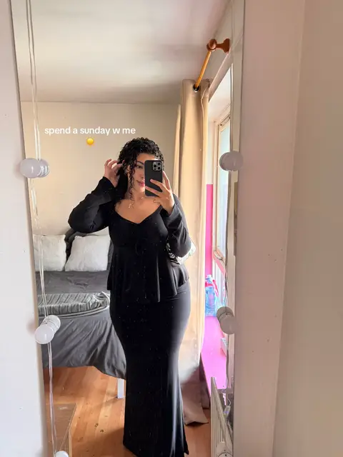 A woman is taking a mirror selfie in a bedroom, she is wearing a long black dress. The mirror has a few decorations and a few light. Text overlay is at the top showing the hook text.