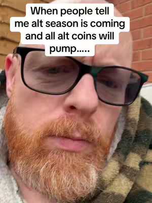 A close-up shot of a red-bearded, bald man wearing large black-framed glasses. The top of the image has white text overlaid on it. The man is wearing a patterned green and brown scarf around his shoulders. His expression is neutral, and the lighting appears natural.