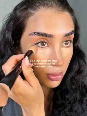 A close-up shot features a person applying concealer under their eye with a makeup brush. Text is overlaid, and the person has dark hair and is looking at the viewer.