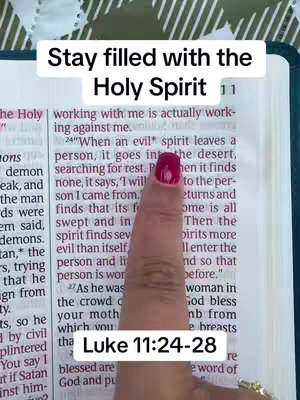 A hand with red nail polish points to text in an open Bible. Above the hand is the text overlay "Stay filled with the Holy Spirit". The pages of the Bible are visible with text, and chapter headings.