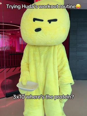 A person in a large yellow costume is standing in an interior setting. Text is superimposed on the image.