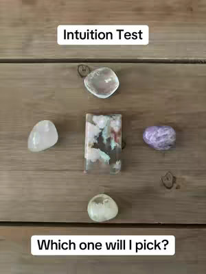 A top-down shot of a wooden surface with five gemstones arranged in a circle. Text overlays read 'Intuition Test' above and 'Which one will I pick?' below, both in white rectangular boxes.