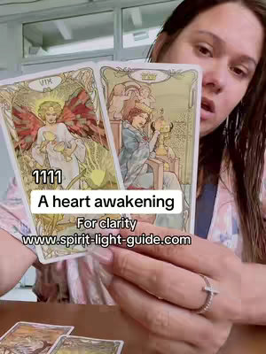 A woman holds two tarot cards in front of her, the cards have a light beige background with illustrations in the background. A text overlay indicates the video is a heart awakening and a website url.