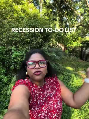 A woman with curly black hair and red-framed glasses is filming herself outdoors with trees in the background. She's wearing a red top with a white floral pattern. Text overlayed reads “Recession to-do List”.