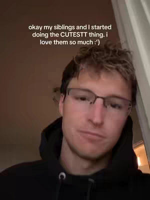 A selfie-style shot features a young man against a blurred backdrop. He is wearing a black hoodie and glasses; his expression is pensive, and he appears to be looking directly at the camera. Text is added at the top.