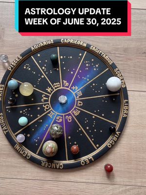 A top-down shot showcases a black, circular astrological wheel set against a pale wooden surface. The wheel is divided into segments, each representing a zodiac sign, and adorned with golden lettering and symbols for each sign. Scattered around the wheel, there are several colorful, spherical gemstones and a few clear crystal spheres. A highlighted band intersects the wheel, highlighting different zones, and the top text reads "ASTROLOGY UPDATE WEEK OF JUNE 30, 2025" in a white box, set against a colored background.