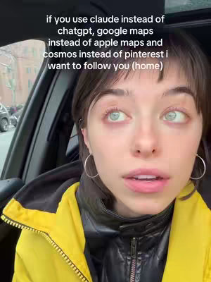 A woman with light skin, short dark hair, and large, light-colored eyes is looking upwards and slightly to the right. She's positioned inside what appears to be a car. She wears hoop earrings, a black leather jacket and a bright yellow overcoat. Text overlaid on the image reads: if you use claude instead of chatgpt, google maps instead of apple maps and cosmos instead of pinterest i want to follow you (home). The background is blurred, suggesting it's a street scene.