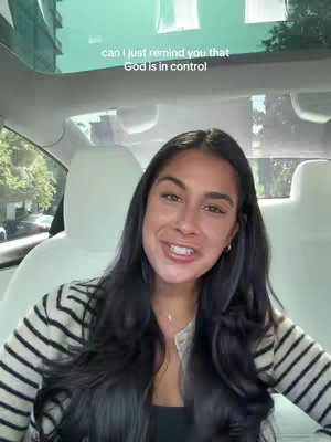 The cover image shows a woman smiling inside a car. She is wearing a striped sweater and a necklace, with long dark hair. The shot is framed from the waist up. The background shows the car's interior - headrests and a sunroof view with natural light filtering through. Text overlay is at the top with the caption 'can I just remind you that
God is in control'.