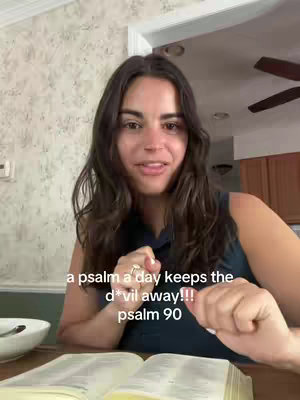 A woman with long, dark hair is seated indoors, partially obscured by a table. She's holding a book open with both hands, with text overlaying on the image.
