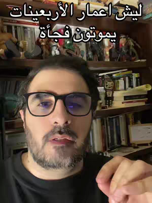 A man with glasses looking at the camera in what seems to be his home. Behind him are shelves of books, and various ornaments.