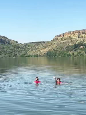 The cover image shows two men swimming in a lake, with hills and a clear sky in the background. Both are wearing red life jackets. One is waving his arm. The water reflects the blue sky. The overall photo has a bright and sunny atmosphere.