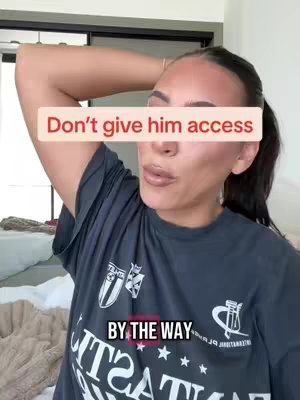 A woman with dark hair and pale skin is shown from the chest up, posing in a medium indoor setting. She wears a dark grey t-shirt and has her right arm reaching to her head. Text overlays state: 'Don't give him access' and 'BY THE WAY'. The background appears to be a home setting with a bed.