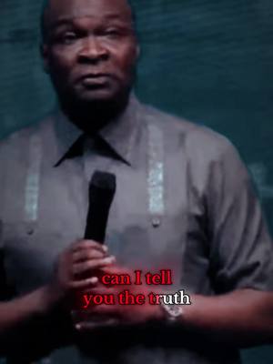 A medium shot of a Black-skinned man wearing a gray shirt, holding a microphone in his hands and looking towards the camera. Overlayed are the words "can I tell you the truth" in red.