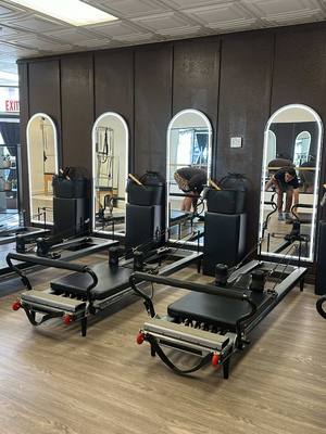 A professional Pilates studio setting with machines and mirrors, with figures in training.