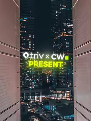 The image is a vertical shot taken at night from inside what seems to be a building, looking out at a cityscape. The frame is created by the light-colored sides of the structure, giving the view a tunnel or window-like appearance. The background is a densely populated area, with many illuminated buildings, windows, and streetlights. The warm glow from the lights contrasts with the dark sky, creating an inviting night ambiance. The image is centered on a text overlay.