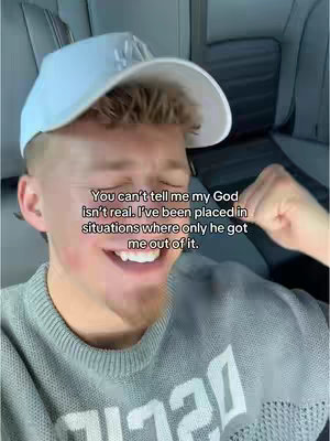 A young man wearing a white cap and gray sweatshirt is captured in a selfie from the shoulders up. The background is softly blurred, but appears to be the interior of a vehicle. Overlaid text conveys personal faith.