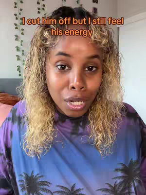 A medium shot features a Black woman with curly blonde-highlighted hair, looking directly at the camera. She is wearing a tie-dye top in shades of blue, purple, and pink, with a palm tree pattern visible. The background is slightly blurred. Text overlay in orange reads 'I cut him off but I still feel his energy'.